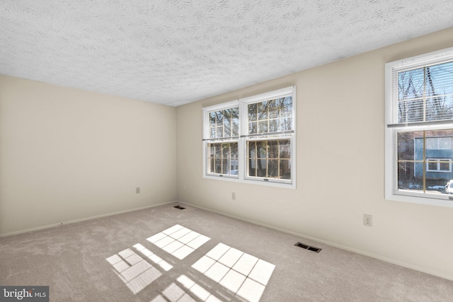 spare room featuring light carpet, baseboards, visible vents, and a textured ceiling