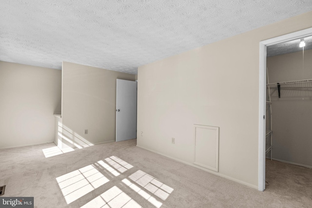 unfurnished bedroom with a textured ceiling, a spacious closet, a closet, and light colored carpet