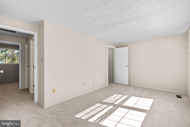 empty room with light carpet, a textured ceiling, visible vents, and baseboards