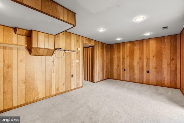 finished below grade area with visible vents, light colored carpet, wooden walls, and baseboards