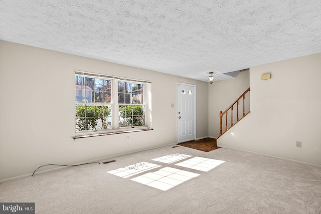 interior space with a textured ceiling, stairs, visible vents, and carpet flooring