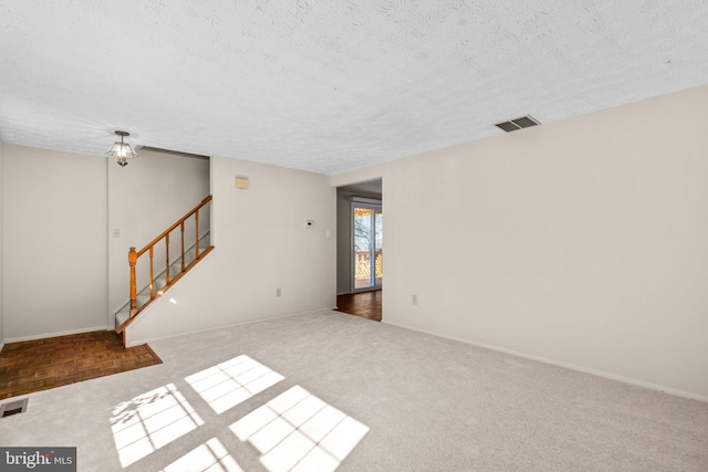 spare room featuring stairs, a textured ceiling, visible vents, and baseboards