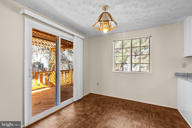 unfurnished dining area featuring a textured ceiling, an inviting chandelier, and baseboards