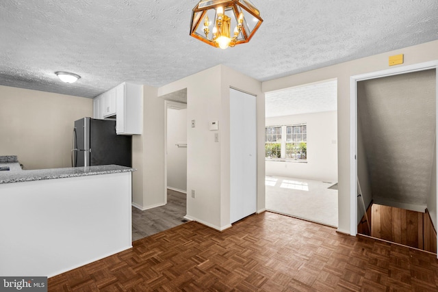 kitchen featuring freestanding refrigerator, light stone countertops, a textured ceiling, white cabinetry, and pendant lighting