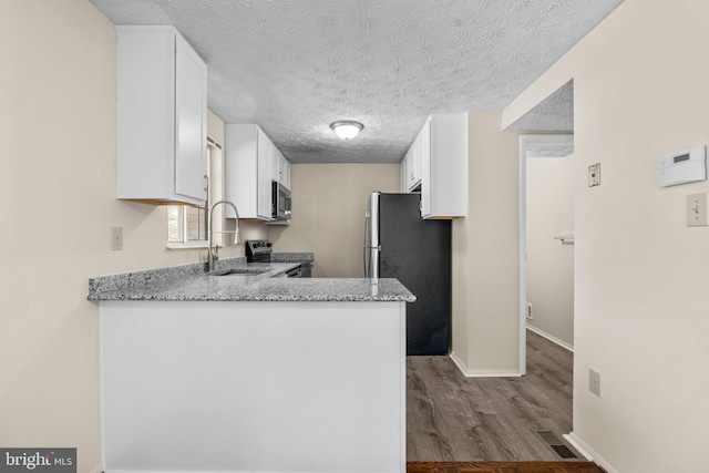 kitchen with appliances with stainless steel finishes, wood finished floors, light stone countertops, white cabinetry, and a sink