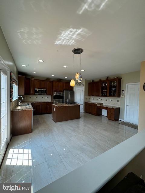 kitchen featuring stainless steel microwave, backsplash, a kitchen island, glass insert cabinets, and refrigerator