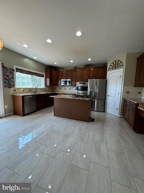 kitchen featuring light stone counters, tasteful backsplash, appliances with stainless steel finishes, and a center island