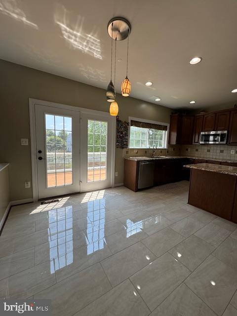 kitchen featuring decorative backsplash, hanging light fixtures, baseboards, and stainless steel appliances