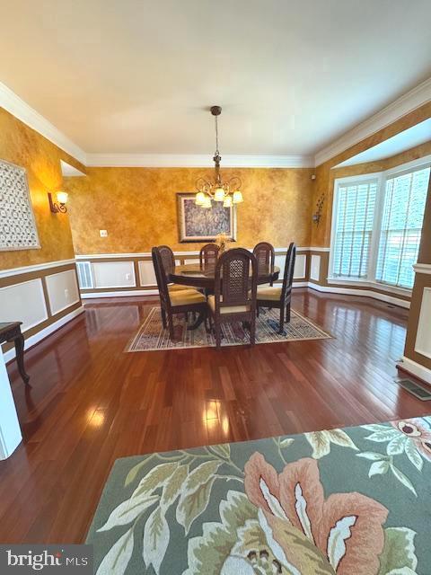 dining room with a wainscoted wall, wood finished floors, an inviting chandelier, crown molding, and a decorative wall