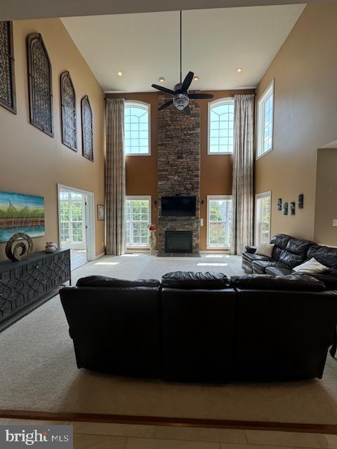 carpeted living area featuring a stone fireplace, plenty of natural light, and a ceiling fan