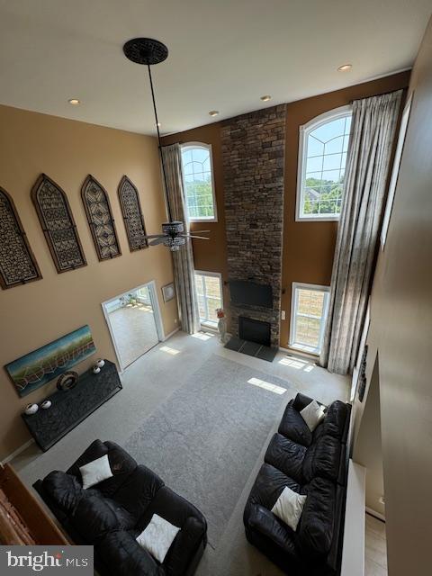 carpeted living area with a stone fireplace, a high ceiling, and a healthy amount of sunlight