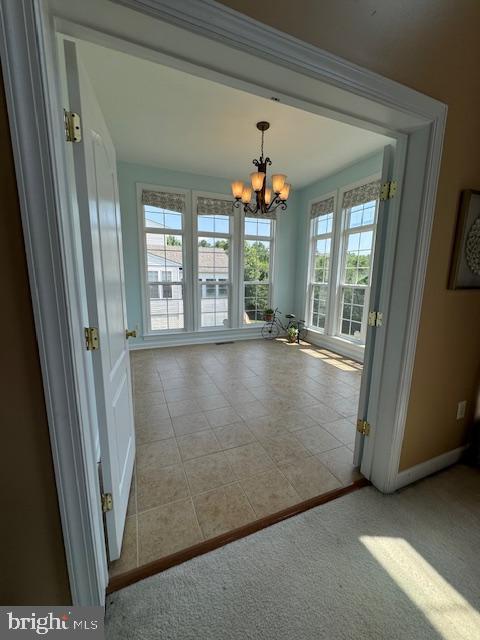 tiled empty room with baseboards, carpet floors, and an inviting chandelier