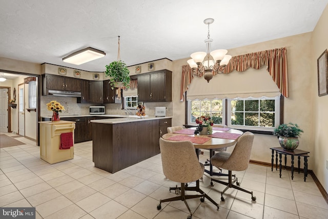 kitchen featuring dark brown cabinetry, tasteful backsplash, stainless steel microwave, a peninsula, and under cabinet range hood