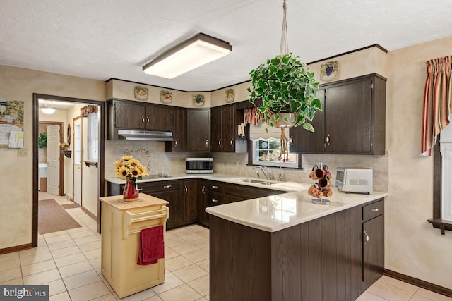 kitchen with stainless steel microwave, a peninsula, light countertops, dark brown cabinets, and backsplash