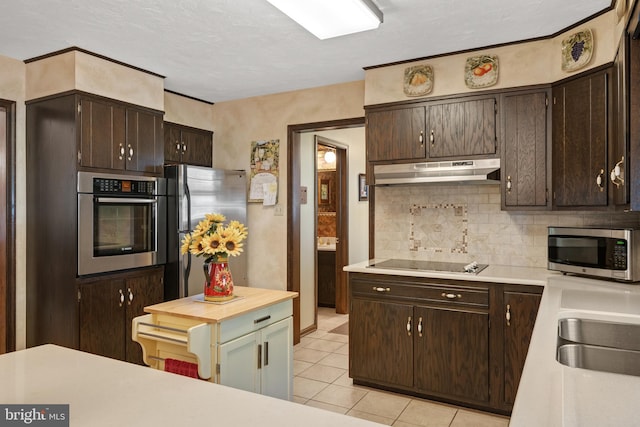 kitchen featuring dark brown cabinetry, under cabinet range hood, light countertops, appliances with stainless steel finishes, and tasteful backsplash