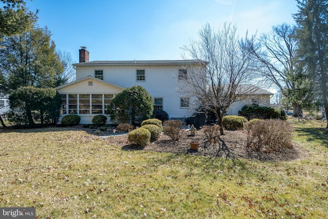 rear view of property featuring a yard, a chimney, and a sunroom