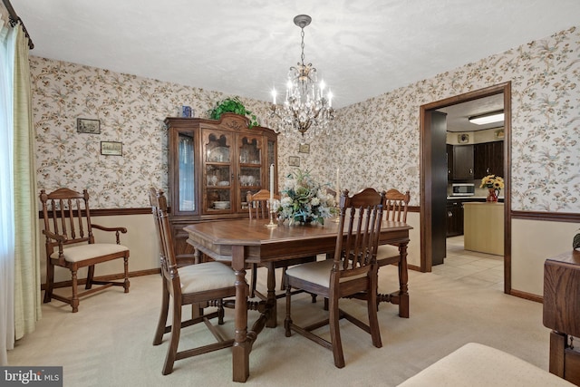 dining area with an inviting chandelier, wainscoting, light colored carpet, and wallpapered walls