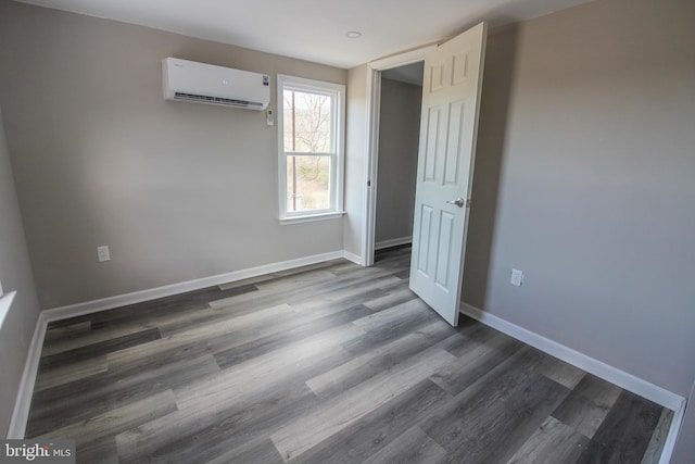 spare room featuring baseboards, dark wood-type flooring, and an AC wall unit