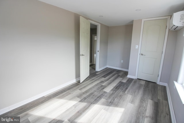 unfurnished bedroom featuring a wall unit AC, baseboards, and wood finished floors