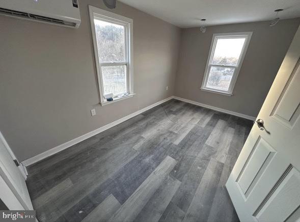unfurnished bedroom featuring dark wood-style flooring, a wall unit AC, and baseboards