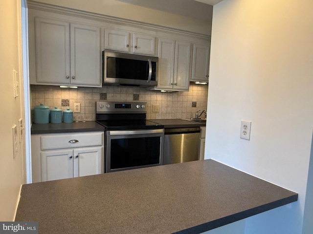 kitchen with a sink, white cabinets, appliances with stainless steel finishes, backsplash, and dark countertops