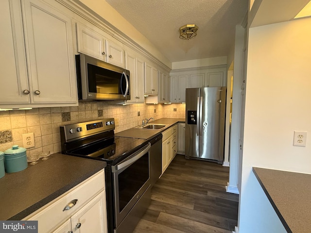 kitchen with stainless steel appliances, dark countertops, white cabinetry, and a sink