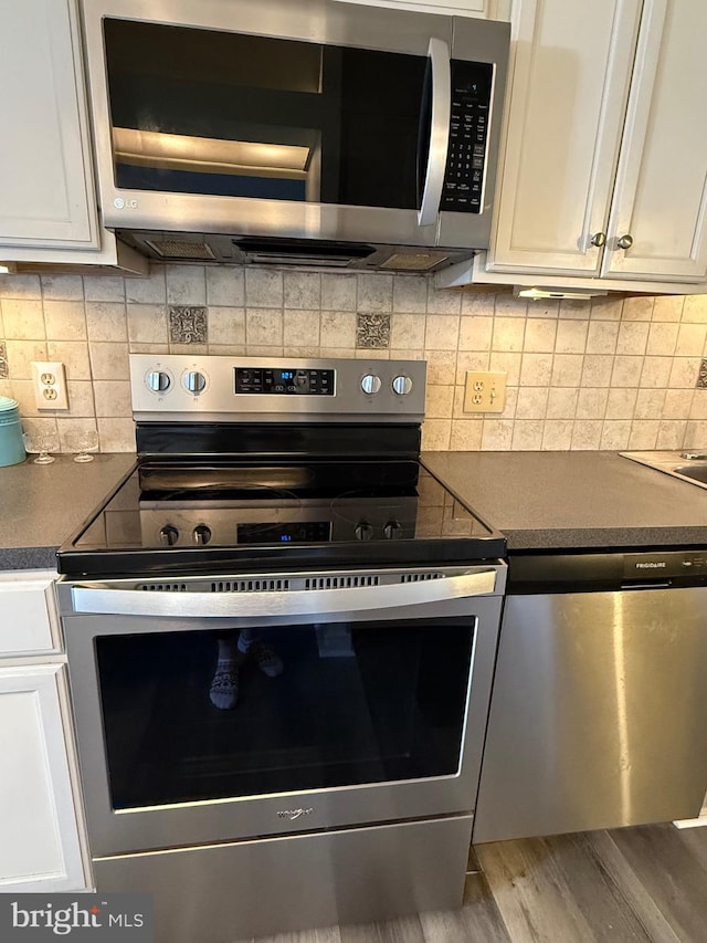 kitchen with tasteful backsplash, white cabinets, dark countertops, wood finished floors, and stainless steel appliances