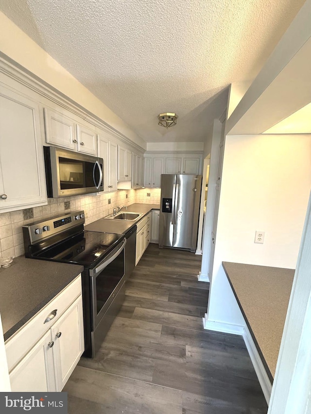 kitchen featuring decorative backsplash, dark countertops, appliances with stainless steel finishes, dark wood-type flooring, and a sink