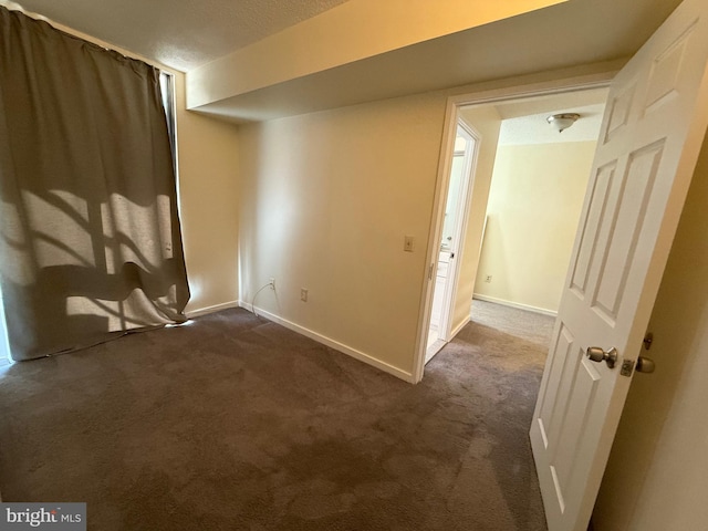 empty room featuring dark colored carpet, a textured ceiling, and baseboards