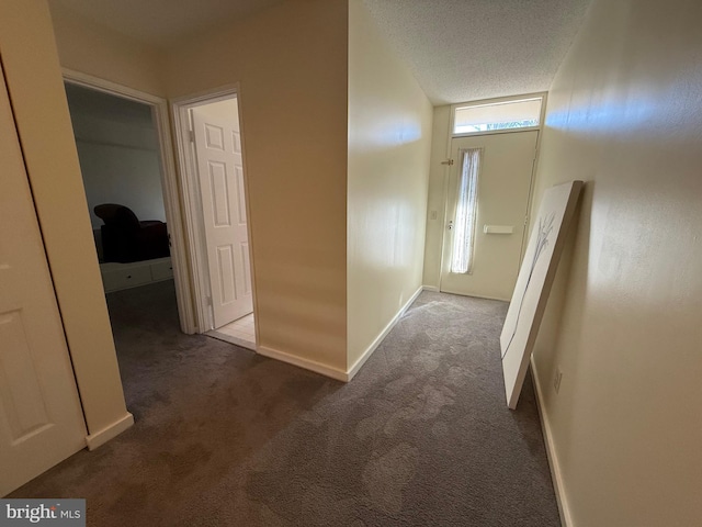 corridor featuring baseboards, dark colored carpet, and a textured ceiling