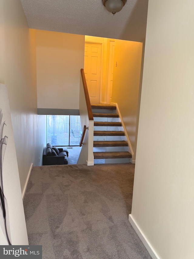 staircase featuring carpet floors, a textured ceiling, and baseboards