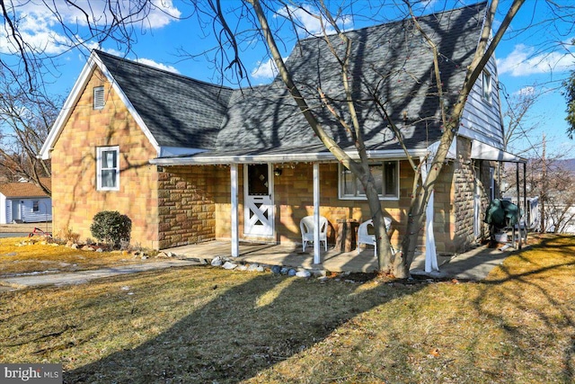 view of front of property featuring stone siding, a shingled roof, a front lawn, and covered porch