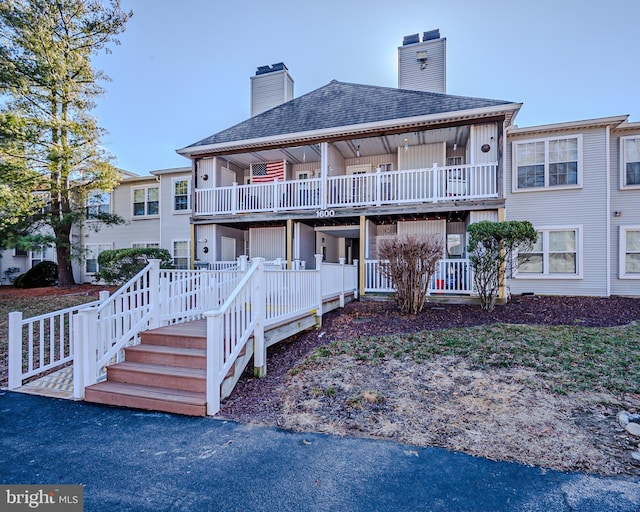 exterior space with roof with shingles, a chimney, and a balcony