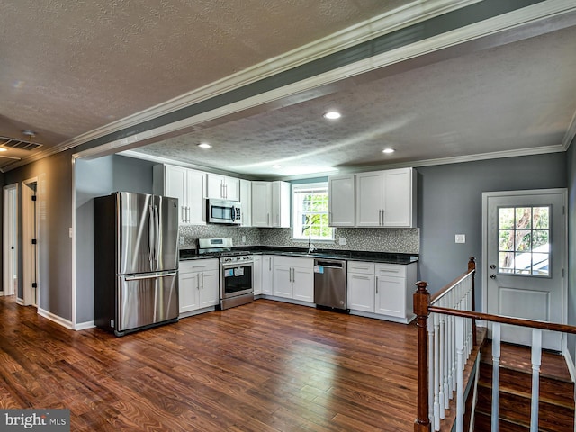 kitchen with dark countertops, dark wood-style flooring, stainless steel appliances, white cabinetry, and backsplash