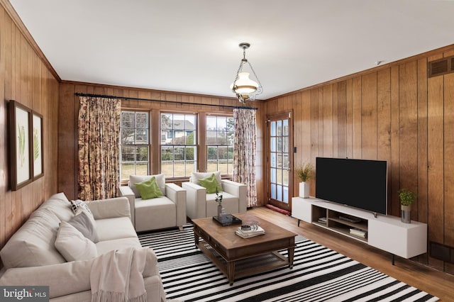 living area with ornamental molding, visible vents, wooden walls, and wood finished floors