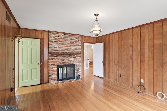 unfurnished living room featuring ornamental molding, a brick fireplace, wood finished floors, and wooden walls