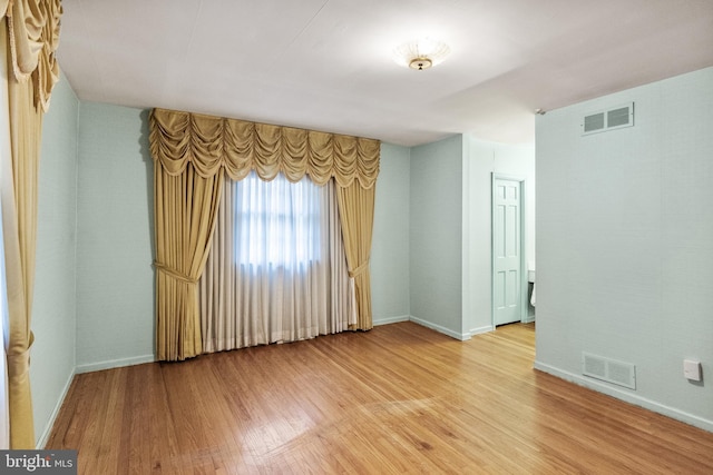 unfurnished room featuring light wood-style flooring, visible vents, and baseboards