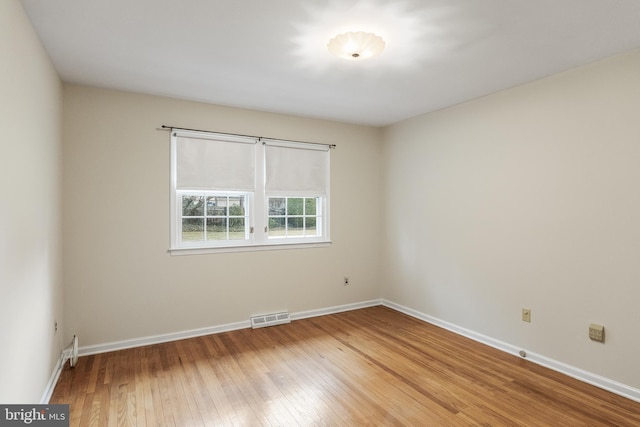 empty room featuring light wood finished floors, visible vents, and baseboards