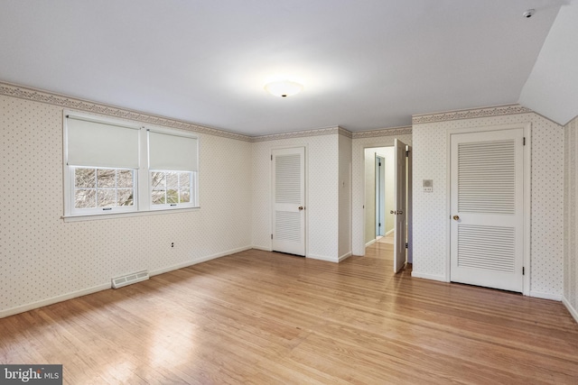 unfurnished bedroom featuring wallpapered walls, light wood-style flooring, visible vents, and two closets