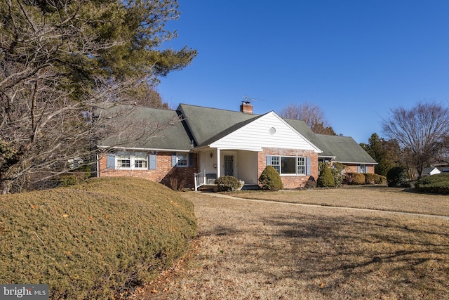 ranch-style house with covered porch, brick siding, a chimney, and a front lawn