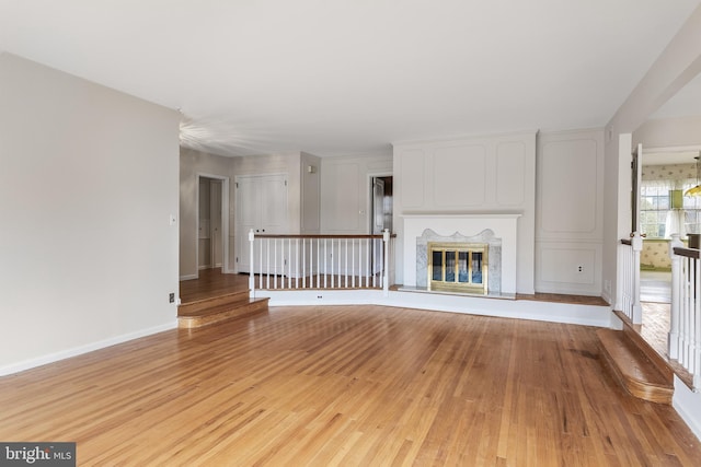 unfurnished living room with light wood-style floors, a glass covered fireplace, and baseboards