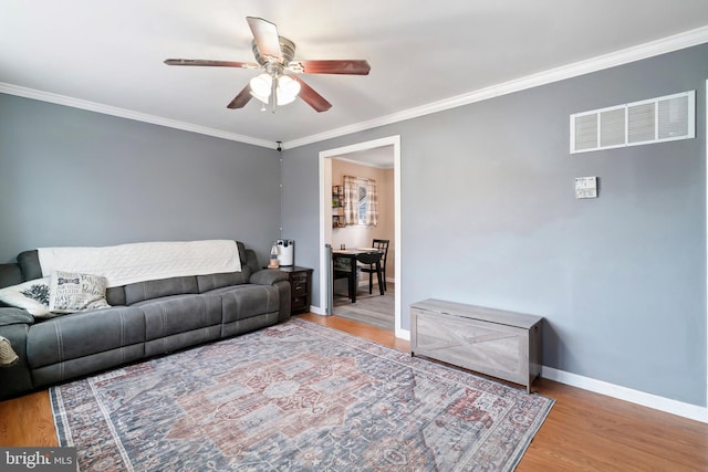 living room featuring ceiling fan, wood finished floors, visible vents, baseboards, and ornamental molding