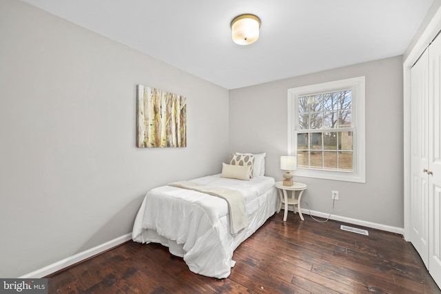 bedroom with baseboards, visible vents, dark wood finished floors, and a closet