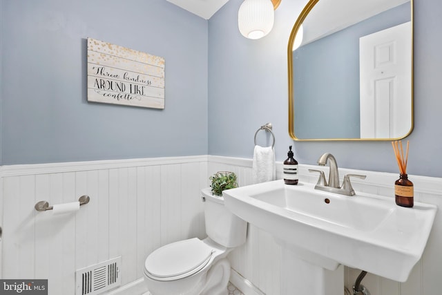 bathroom featuring toilet, a wainscoted wall, visible vents, and a sink