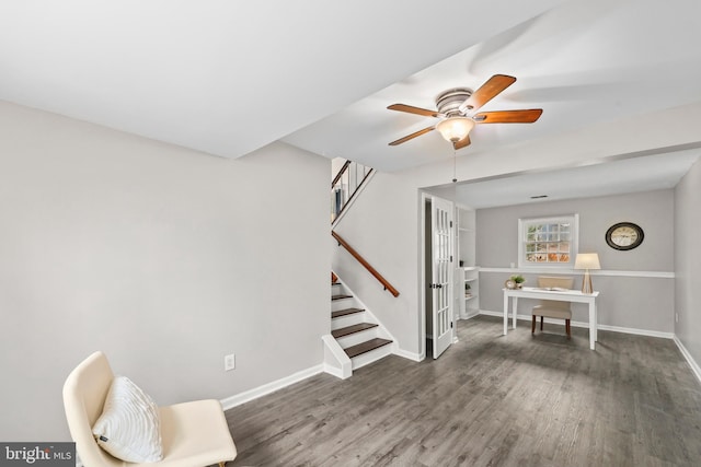 sitting room featuring stairs, dark wood finished floors, a ceiling fan, and baseboards