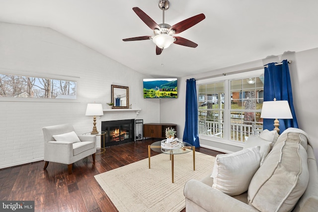 living area featuring lofted ceiling, a glass covered fireplace, dark wood finished floors, and a ceiling fan