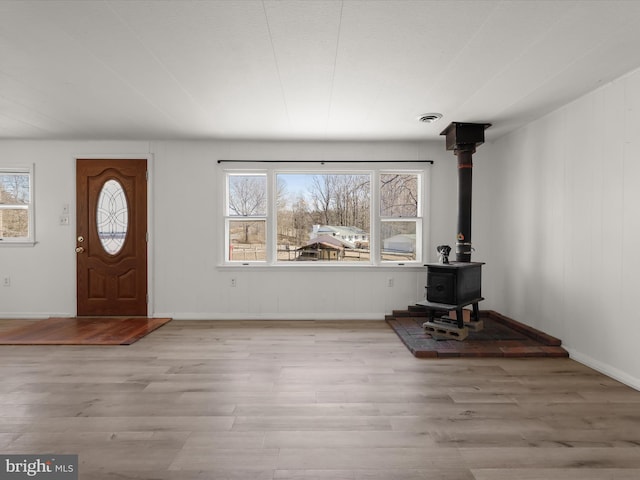 foyer featuring wood finished floors, a wood stove, a healthy amount of sunlight, and visible vents