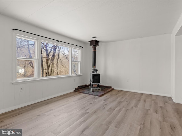 unfurnished living room with a wood stove, baseboards, and wood finished floors