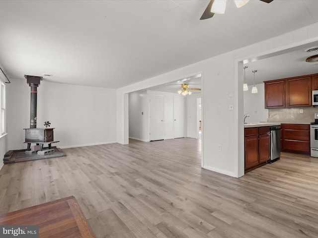 unfurnished living room featuring light wood-type flooring, baseboards, a ceiling fan, and a wood stove