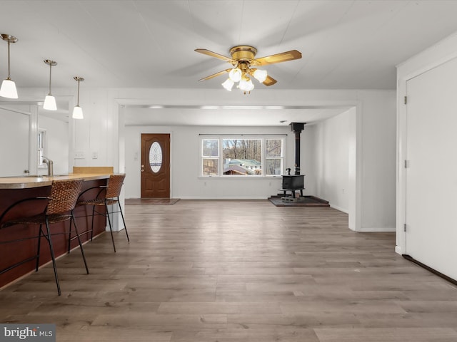 interior space featuring a ceiling fan, a wood stove, wood finished floors, and baseboards